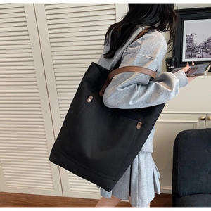 Side view of large black canvas tote bag with brown leather straps worn by model