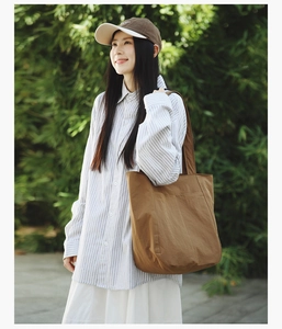 Brown large capacity tote bag worn with a striped shirt in a natural outdoor setting