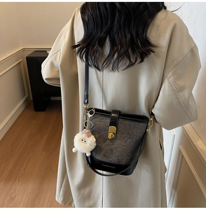 Détail du sac seau gris avec fermoir doré, breloque en peluche et texte de mode