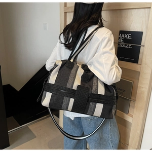 Close-up of striped canvas travel tote featuring double handles and a zip pocket on a model