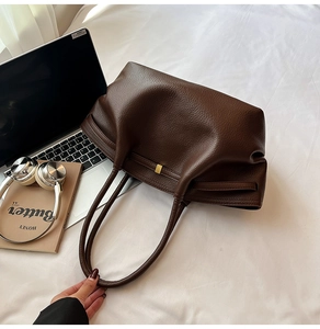 Detail of dark brown pebble leather tote bag featuring a polished gold square buckle