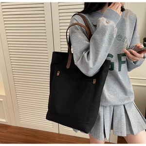 Detail of a large black canvas tote bag with brown leather handles worn by a model