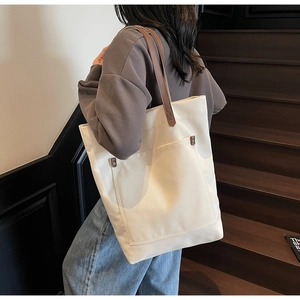 Detail of canvas tote bag with brown leather straps and metal rivets on wood stairs