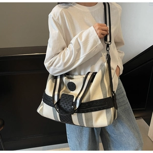 Detail of striped travel bag with black leather trim and woven adjustable shoulder strap