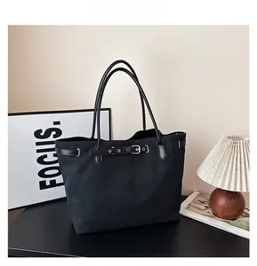 Detail of a large black canvas tote bag with leather straps and metal buckle decoration