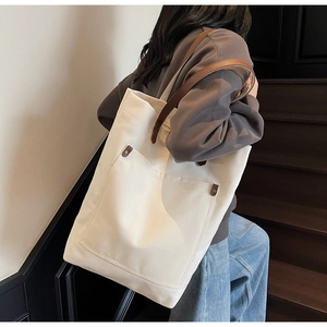 Detail of canvas tote bag with brown leather handles and bronze rivets on exterior pocket