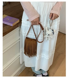 Détail d'un petit sac à bandoulière marron à franges avec un porte-clés ours blanc peluche