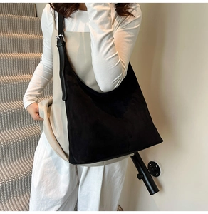 Detail of minimalist black suede hobo bag featuring adjustable leather shoulder strap