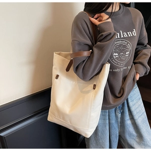 Chic beige canvas tote bag with brown leather handles worn by model in a casual setting