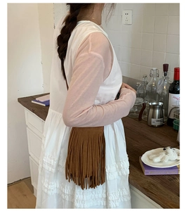 Détail d'un sac à bandoulière marron foncé à franges porté avec une robe blanche à volants