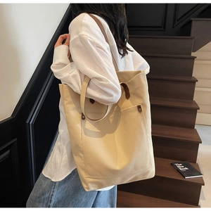 Detailed view of minimalist off-white canvas tote bag with brown leather accents on stairs