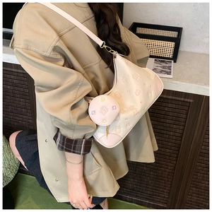 Detail of beige shoulder bag featuring embossed bear pattern and circular coin purse attachment