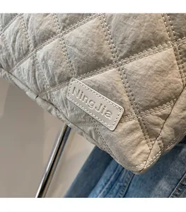Close-up of beige quilted fabric and leather brand tag on a modern tote bag