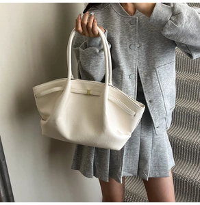 Detail view of cream tote bag featuring textured leather and a minimalist gold clasp