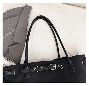 Detail of black canvas tote bag showing faux leather handles and silver metal buckles