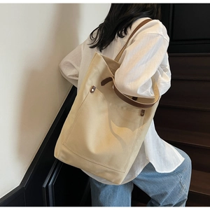 Detail of canvas tote bag with brown leather handles and decorative rivets on outer pocket