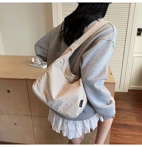 Side view of cream canvas hobo bag with a minimalist logo tag worn by a model