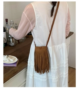 Gros plan sur un sac bandoulière marron à franges porté sur une élégante robe blanche