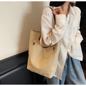Detail of large beige canvas tote bag with brown leather straps and front pocket