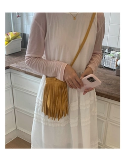 Détail du sac bandoulière jaune à franges en daim porté par un mannequin en extérieur