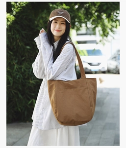 Outdoor street view of a large brown canvas tote bag with front pocket and wide strap