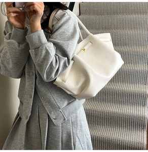 Close-up of white lychee leather tote bag featuring gold hardware and side buckles