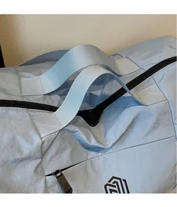 Detail of light blue nylon travel bag showing reinforced gray handle and smooth fabric texture