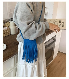 Détail d'un petit sac bandoulière bleu vif avec franges sur un sweat gris