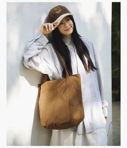 Brown canvas tote bag with wide strap and outer pocket shown in outdoor lifestyle setting