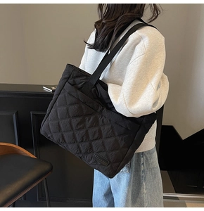 Close-up of black quilted nylon tote bag with rhombus stitching and brand label detail