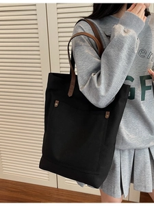 Minimalist black canvas tote bag with brown leather handles and front pocket shown on model