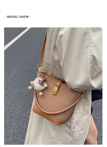 Secchiello in pelle opaca marrone con chiusura dorata e peluche su un trench beige