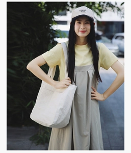 Outdoor shot of a beige large canvas tote bag styled with a yellow tee and pinafore dress