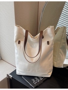 Minimalist large canvas tote bag with brown leather straps and vintage rivets in a home setting