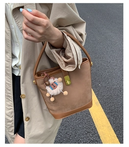 Close-up of brown matte bucket bag with gold metal clasp and plush sheep charm
