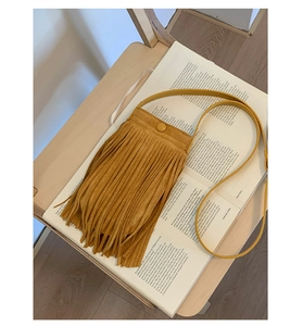 Détail du sac à bandoulière moutarde à franges posé sur un livre ancien