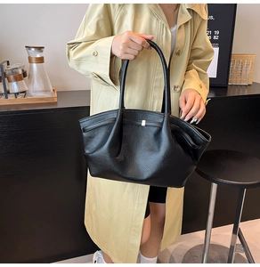 Detail of black lychee grain leather tote bag with side pleats and golden metal fastener