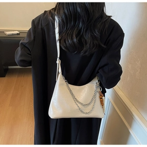 Detail view of stylish beige crescent bag with silver chains and ethnic bead pendant
