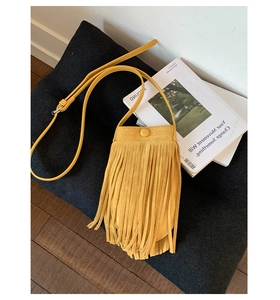 Détail d'un sac bandoulière jaune à franges sur un coussin noir avec un livre d'art