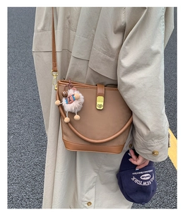 Detail einer braunen Leder-Eimertasche mit goldenem db-Verschluss und Plüschtieranhänger