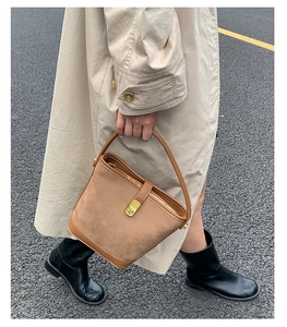 Brown suede bucket bag with gold metal clasp carried by model in beige trench coat
