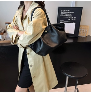 Detail of black pebbled leather tote bag with gold metal buckle on casual trench coat