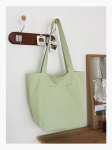 Detail of light green canvas tote bag featuring a front pocket hanging on a wooden hook
