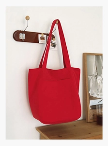 Detail of red canvas tote bag with large front pocket hanging on a wooden hook
