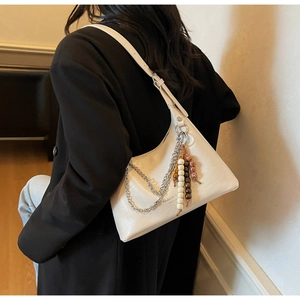 Detail of cream hobo underarm bag featuring silver chains and ethnic tassel pendant