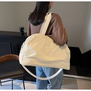 Close-up of cream travel bag with NINGJIA logo and adjustable shoulder strap worn by model