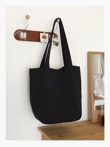 Detail shot of large black canvas tote bag hanging on wooden hook against white wall