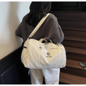 Detail of cream travel bag with adjustable strap worn by a model on stairs