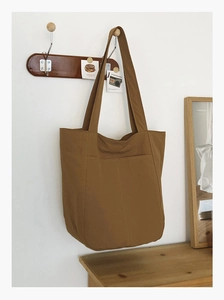 Close-up of khaki canvas tote bag hanging on wooden hook in a minimalist home setting
