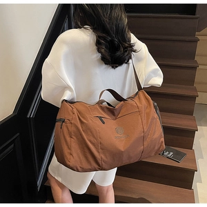 Brown travel bag with shoulder strap shown carried by a model on wooden stairs